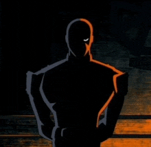 a silhouette of a man in a black and orange costume is standing in the dark .