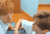 two boys are looking at each other and one has a phone that says iphone