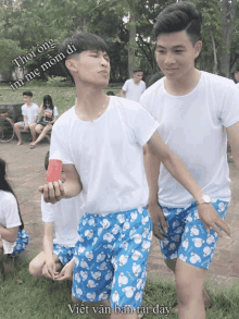 a man in a white shirt and blue shorts holds a piece of watermelon in his hand