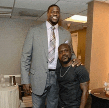 a man in a suit and tie is standing next to another man in a black shirt