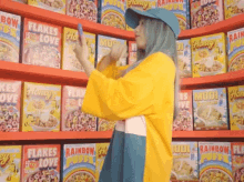 a woman is standing in front of a shelf of cereal boxes including flakes of love and rainbow puffs .