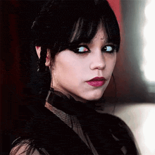 a woman with black hair and red lips is wearing a black dress and choker .