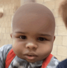 a baby with a bald head is wearing a camouflage outfit