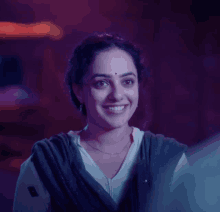 a woman with a bindi on her forehead smiles in a dark room