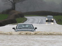 two cars are driving down a flooded road one of which has a license plate that starts with the letter g