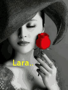 a woman wearing a hat is holding a red rose in her hand .