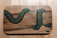 a painting of a snake on a wooden cutting board with the name miller written on the bottom