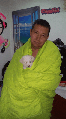 a man wrapped in a green blanket holds a small white puppy