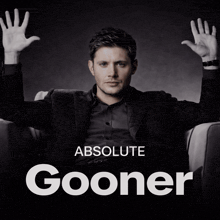 a man in a suit sits in a chair with his hands in the air and absolute gooner is written above him