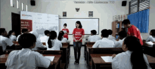 a woman in a red shirt that says mufg on it stands in front of a classroom full of students