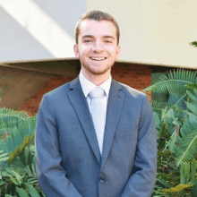 a young man in a suit and tie is smiling while standing in front of a brick building .