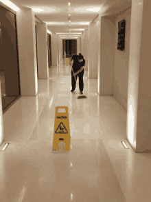 a man cleaning a hallway with a yellow caution sign