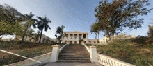 a large white building with stairs leading up to it is surrounded by trees and grass .