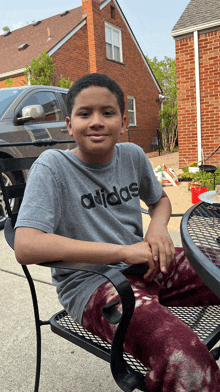 a young boy wearing an adidas shirt sits at a table outside