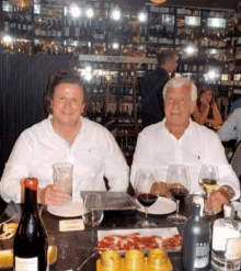 two men sit at a table with wine glasses and a sign that says bodega in the background