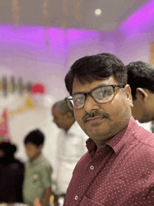 a man wearing glasses and a red shirt stands in front of a purple background