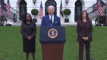 the president of the united states is giving a speech at a podium with two women standing behind him .