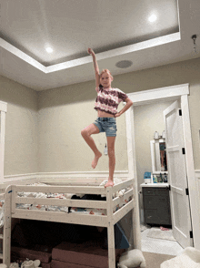 a young girl stands on a bunk bed with her arms outstretched