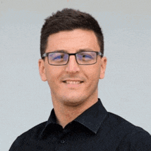 a young man wearing glasses and a black shirt is smiling .