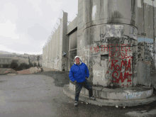 a man in a blue jacket stands in front of a wall that has graffiti on it including one that says " vwiz "