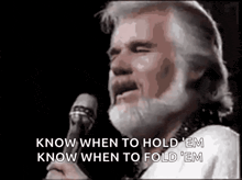 a man with a beard is singing into a microphone and says `` know when to hold em know when to fold em ''
