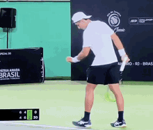 a man in a white shirt and black shorts is playing tennis in front of a banner that says brasil