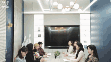 a group of women sit around a table in a conference room with twice written on the wall behind them