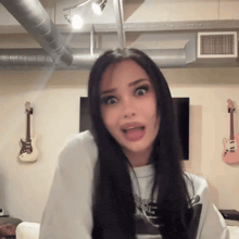 a woman with a surprised look on her face is standing in front of a wall with guitars hanging on it