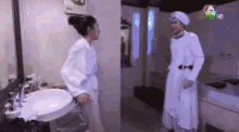 a woman in a bathrobe is standing next to a man in a white robe in a bathroom .