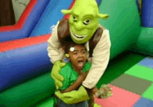 a shrek mascot is hugging a little girl