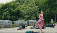 a woman in a pink dress is standing in the middle of a street with people laying on the ground