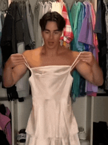 a man is holding a white dress in front of a closet full of clothes .