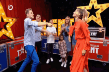 a woman in a red dress is dancing with a group of people in front of a sign that says talent