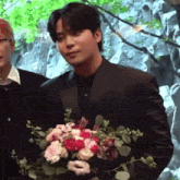 a man in a suit is holding a bouquet of flowers in his hand .
