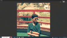 a computer screen shows a picture of a young man sitting on a balcony with his arms crossed