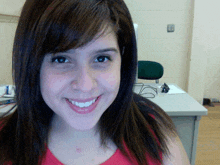 a woman in a red shirt smiles for the camera in front of a desk