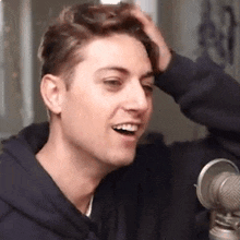 a young man is sitting in front of a microphone and smiling while holding his hair .