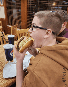 a boy is eating a hamburger with a pepsi cup in the background