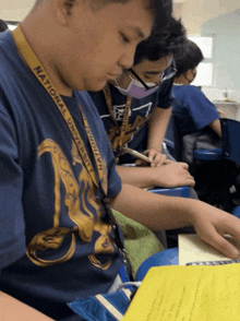 a boy wearing a national university lanyard sits at a desk