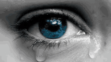 a close up of a woman 's blue eye with a tear coming out of it in a black and white photo .