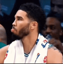 a basketball player with a beard and a towel around his neck is sitting in the stands during a game .