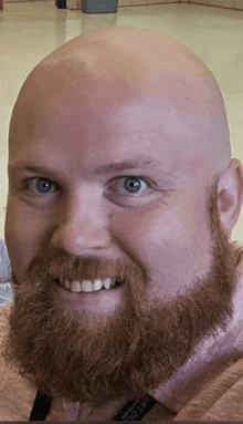 a bald man with a red beard and blue eyes is smiling .