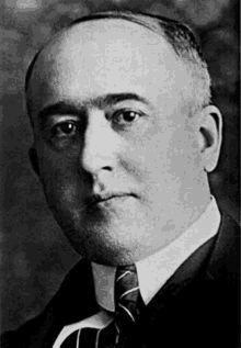 a black and white photo of a man wearing a suit and tie .