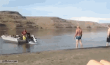 a group of people are standing on a beach next to a boat that is going down the water .