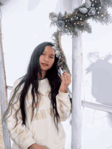 a woman in a white sweater holds a christmas wreath in her hand