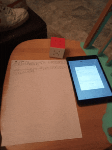 a tablet sits on a wooden table next to a piece of paper that says 2m5bpasbsrmblc