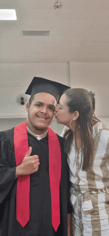 a woman kisses a graduate on the cheek while he gives a thumbs up