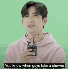 a man wearing a pink hoodie is holding a microphone and says you know when guys take a shower