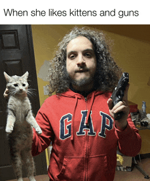 a man holding a cat and a gun wearing a red gap sweatshirt