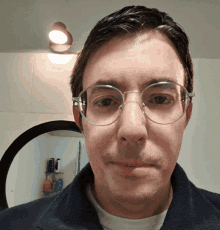 a man wearing glasses looks at the camera in front of a bathroom mirror